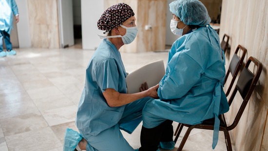 Doctor in scrubs and mask kneeling with patient, also in scrubs and mask